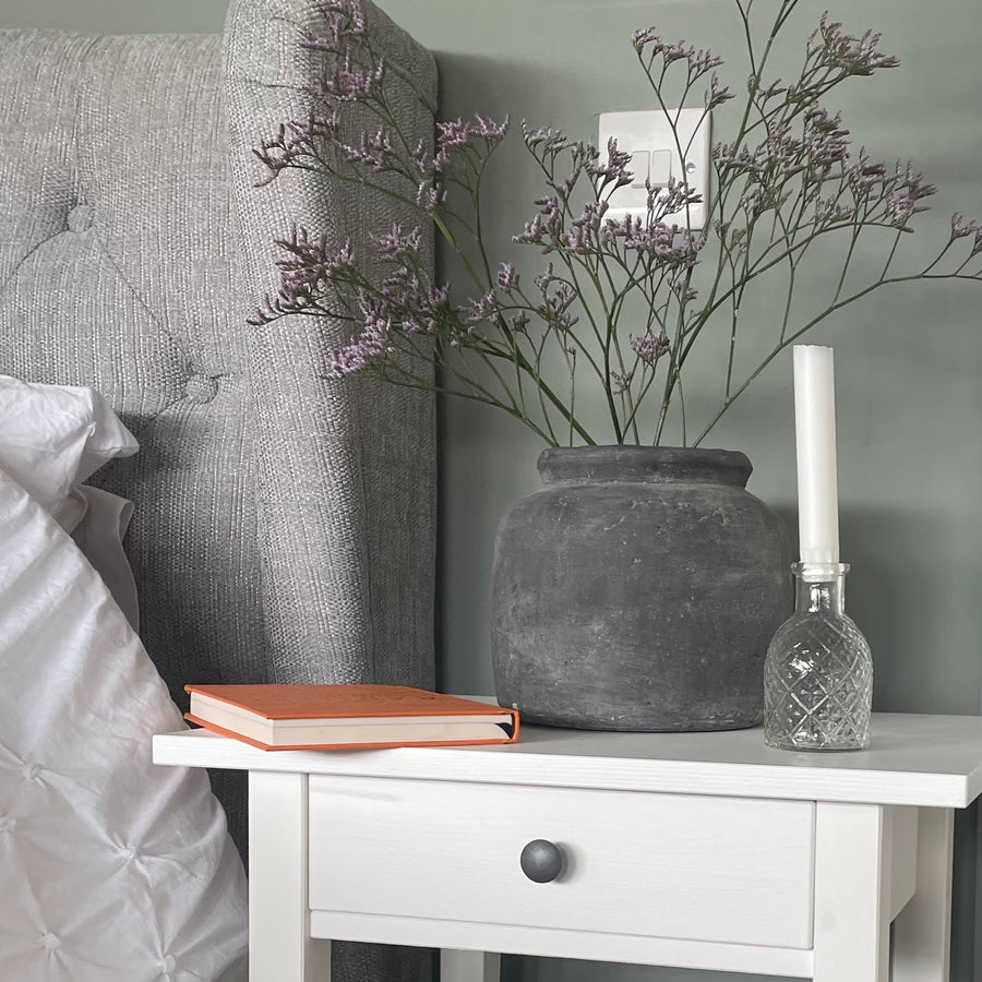 Grey concrete planter with flowers styled on a bed side table